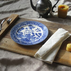 May include: A wooden serving tray with a blue and white patterned plate, a white napkin, and two small yellow candles. The tray has a metal handle.
