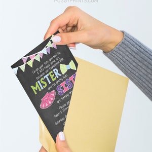 Op de afbeelding: Een uitnodiging in krijtbord-stijl met een kleurrijk lint en de tekst "Mister and his pretty twin Sister are turning one". De uitnodiging zit in een gouden envelop.