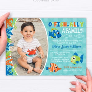 May include: A blue and green invitation with a photo of a baby boy in a red and orange crab onesie. The invitation says "O'Fish-Ally A Family!" and includes the text "Please join us in celebrating the adoption of our son Oliver Jacob Williams" and details for the event.