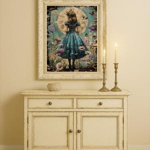 Op de afbeelding: Een ingelijst kunstwerk dat een meisje in een blauwe jurk voor een klok afbeeldt, omringd door bloemen. Het kunstwerk hangt boven een cr&egrave;mekleurige kast met twee lades en twee deuren. Twee brandende kaarsen in messing houders staan op de kast.