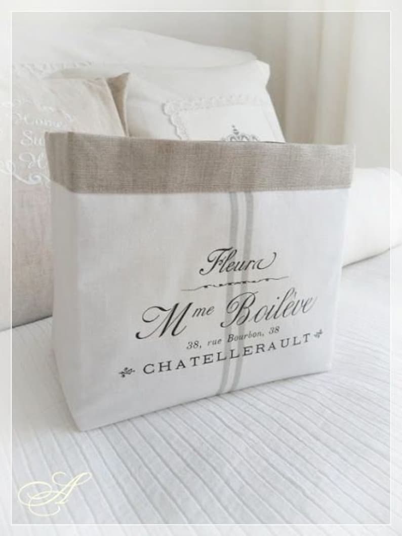 Puede incluir: Una bolsa de almacenamiento de lino blanco con un borde de lino beige. La bolsa presenta el texto "Fleur Mme Boil&egrave;ve" y "38, rue Bourbon, CHATELLERAULT" en escritura negra. Dos rayas verticales grises recorren la parte delantera.