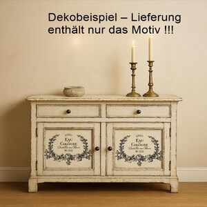 Puede incluir: Un aparador blanco roto envejecido con dos cajones y dos puertas. Las puertas presentan un dise&ntilde;o floral en blanco y negro con el texto "EAU COLOGNE". Dos candelabros de lat&oacute;n con velas encendidas y un peque&ntilde;o cuenco tejido est&aacute;n encima. El texto "Dekobeispiel - Lieferung enth&auml;lt nur das Motiv !!!" est&aacute; en la parte superior.