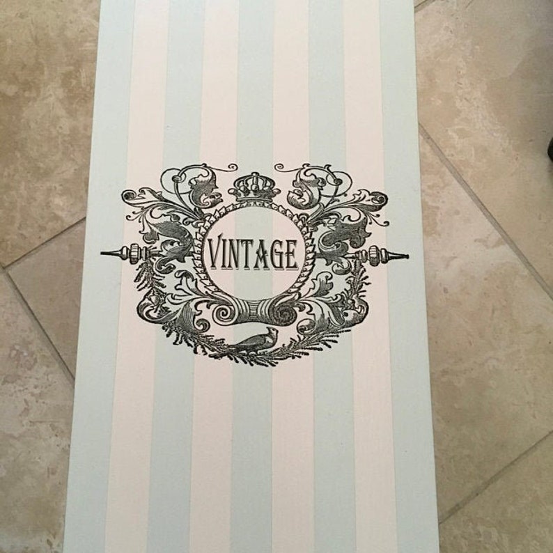 May include: A rectangular box with a light blue and white striped pattern. The box features a decorative black and white vintage emblem with the word "VINTAGE" in a circular frame.