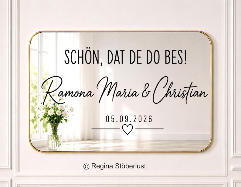 May include: A rectangular mirror with a thin gold frame featuring black text that reads SCH&Ouml;N, DAT DE DO BES!, Ramona Maria & Christian, and the date 05.09.2026 with a small heart icon centered below the date.