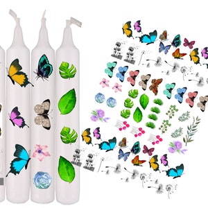 May include: Four white candles decorated with colorful butterfly and floral decals. The butterflies are in various colors, including yellow, blue, pink, and brown. Additional decals include green leaves, flowers, and dandelion illustrations. The candles are arranged vertically.