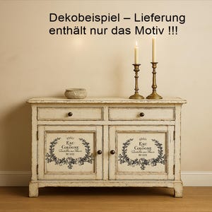 Puede incluir: Un aparador blanco roto envejecido con dos cajones y dos puertas. Las puertas presentan un dise&ntilde;o floral en blanco y negro con el texto "EAU COLOGNE". Dos candelabros de lat&oacute;n con velas encendidas y un peque&ntilde;o cuenco tejido est&aacute;n encima. El texto "Dekobeispiel - Lieferung enth&auml;lt nur das Motiv !!!" est&aacute; en la parte superior.