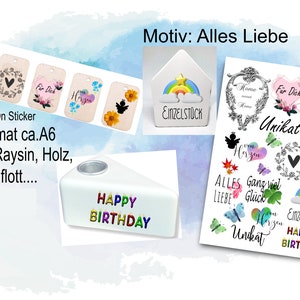 Könnte beinhalten: Eine Sammlung von Aufklebern und Dekorationsartikeln. Enthält Rub-On-Sticker mit Blumen- und Herzmotiven, einen kleinen hausförmigen Behälter mit einem Regenbogen und einen weißen Kerzenhalter mit "HAPPY BIRTHDAY" in bunten Buchstaben. Der Text "Motiv: Alles Liebe" ist ebenfalls sichtbar.