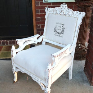 Puede incluir: Sill&oacute;n blanco envejecido con asiento y respaldo de lino. La parte trasera de la silla presenta un dise&ntilde;o impreso con las palabras "GRAINS" y "Aix Les Bains". La silla tiene detalles tallados y reposabrazos ornamentados.