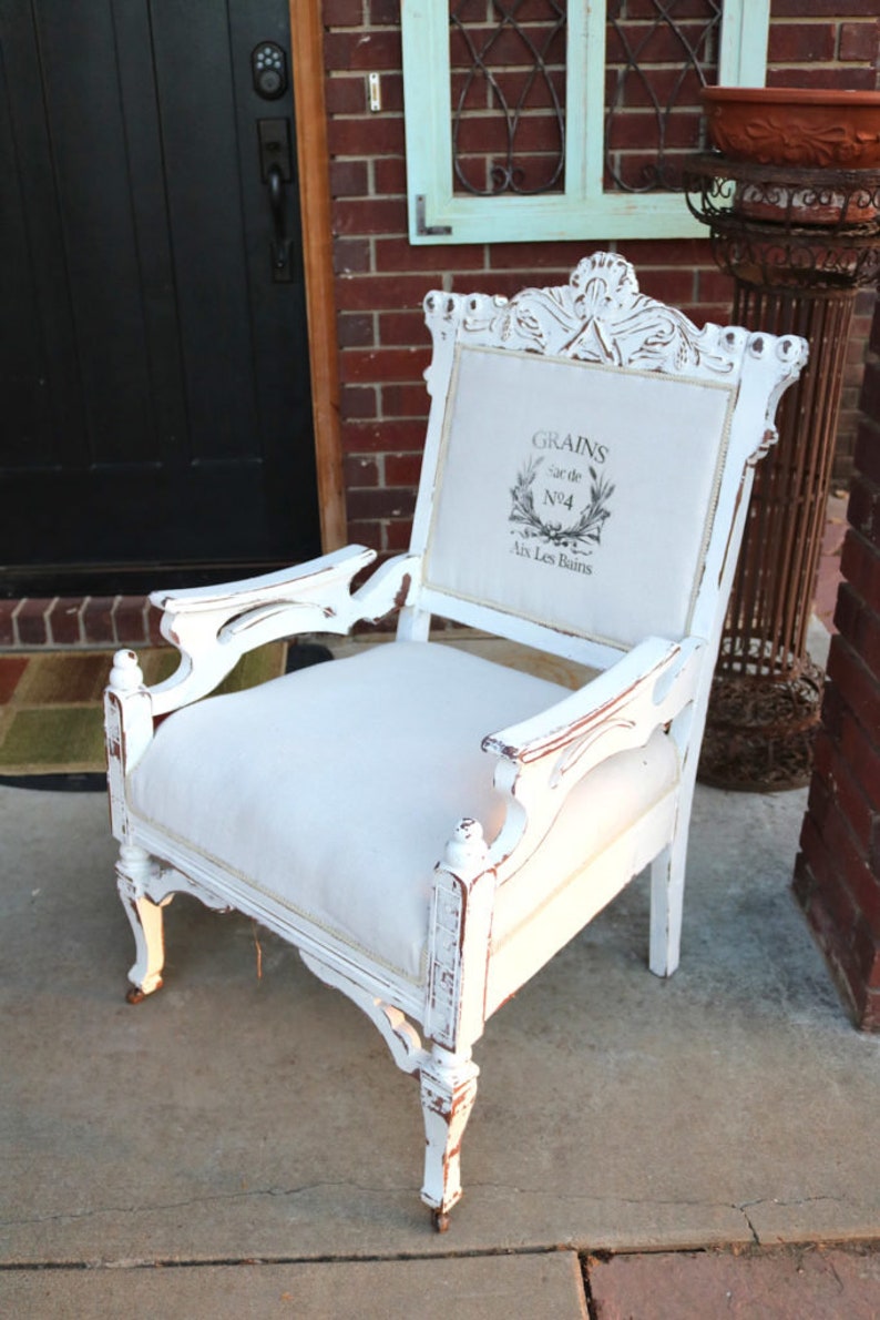 Puede incluir: Sill&oacute;n blanco envejecido con asiento y respaldo de lino. La parte trasera de la silla presenta un dise&ntilde;o impreso con las palabras "GRAINS" y "Aix Les Bains". La silla tiene detalles tallados y reposabrazos ornamentados.