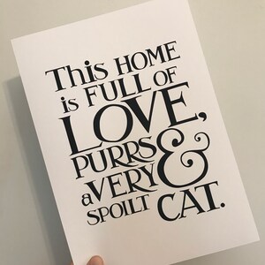 May include: Black and white typography print with the text "This home is full of love, purrs & a very spoilt cat."