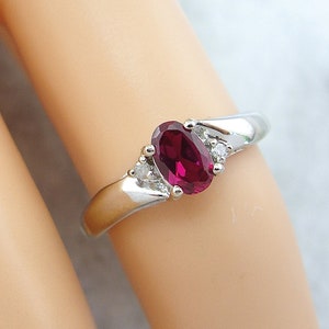 May include: A silver ring with a large oval-shaped ruby gemstone and smaller diamond accents.