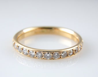 Puede incluir: Un anillo de banda de oro con una fila de pequeños diamantes engastados en la banda.