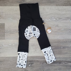 May include: Black leggings with a white patch on the back featuring a black and white print of a fox, mountains, trees, and the text "Run Wild Child". The leggings have white cuffs with the same print.