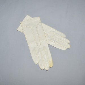 May include: A pair of white leather gloves with decorative stitching. The gloves are folded in half and the fingers are pointing towards the right side of the image.