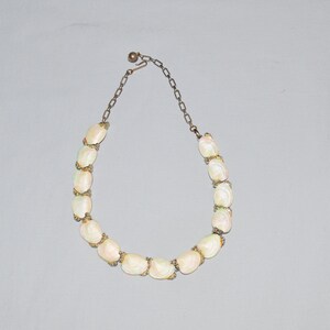 May include: A white shell necklace with a silver chain. The necklace is made of oval-shaped shells with a pearly finish.