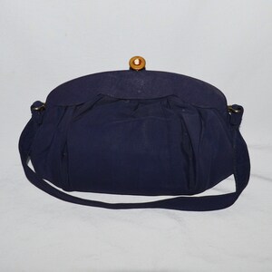 May include: A navy blue handbag with a gold clasp and a wooden button. The bag has a long strap and a gathered design.