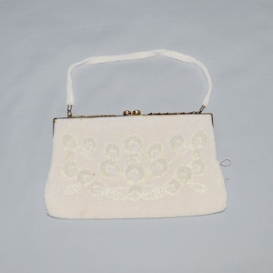 May include: A white beaded evening bag with a gold clasp and a white strap. The bag has a floral design.