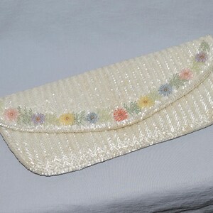 May include: A white beaded clutch purse with a floral design in shades of pink, yellow, and blue.