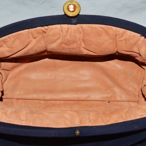 May include: The inside of a navy blue fabric handbag with a peach-colored lining. The handbag has a gold button closure and the lining has the text "Made in France" printed on it.