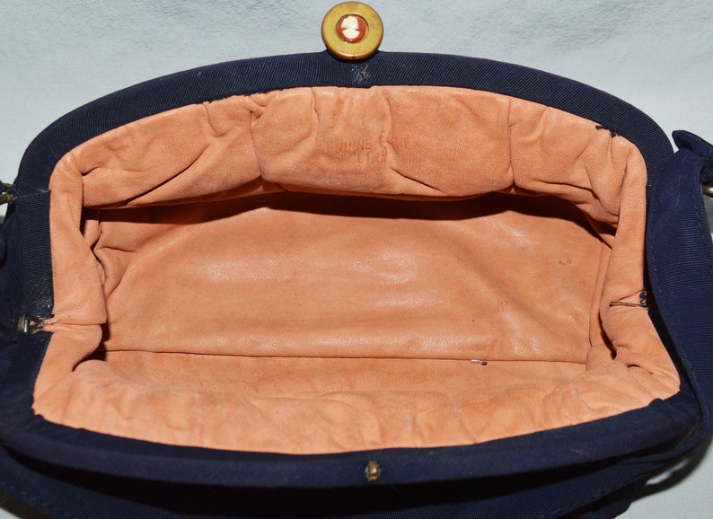 May include: The inside of a navy blue fabric handbag with a peach-colored lining. The handbag has a gold button closure and the lining has the text "Made in France" printed on it.