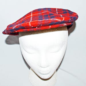Puede incluir: Gorra plana a cuadros rojos con detalles en azul marino y blanco. La gorra se muestra sobre una cabeza de maniqu&iacute; blanca. El patr&oacute;n de cuadros es un dise&ntilde;o cl&aacute;sico, adecuado para varios estilos. La visera de la gorra est&aacute; ligeramente curvada.
