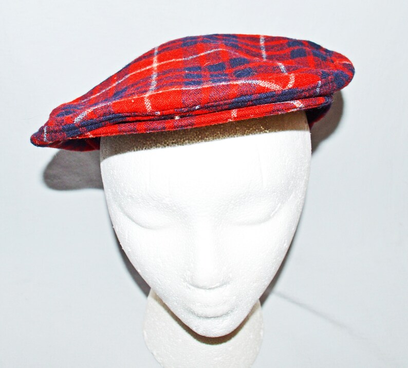 Puede incluir: Gorra plana a cuadros rojos con detalles en azul marino y blanco. La gorra se muestra sobre una cabeza de maniqu&iacute; blanca. El patr&oacute;n de cuadros es un dise&ntilde;o cl&aacute;sico, adecuado para varios estilos. La visera de la gorra est&aacute; ligeramente curvada.
