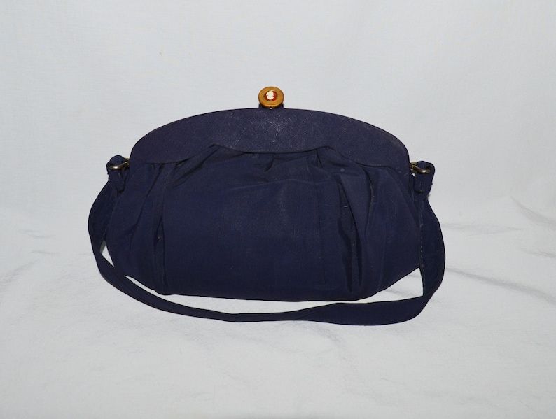 May include: A navy blue handbag with a gold clasp and a wooden button. The bag has a long strap and a gathered design.