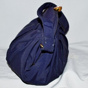 May include: A dark blue fabric handbag with a single gold button closure. The bag is folded and has a textured surface.