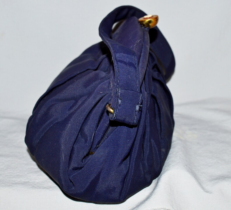 May include: A dark blue fabric handbag with a single gold button closure. The bag is folded and has a textured surface.