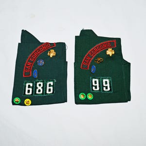 May include: Two green fabric patches with embroidered text "SAN GORGONIO" and numbers "686" and "99". The patches have gold and blue pins attached.