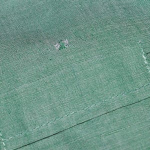 May include: A close-up of a green fabric with a small hole in the centre. The fabric has a pocket with a stitched edge.
