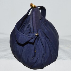 May include: A dark blue fabric handbag with a gold clasp and a gold handle. The bag is folded and has a textured surface.