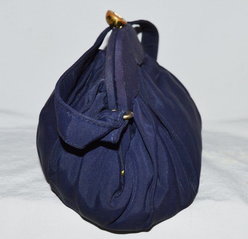 May include: A dark blue fabric handbag with a gold clasp and a gold handle. The bag is folded and has a textured surface.