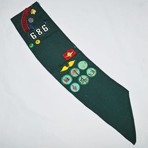 May include: Green Girl Guide sash with various embroidered badges, including a troop number "686", a "Star Gorgeno" badge, and several merit badges.