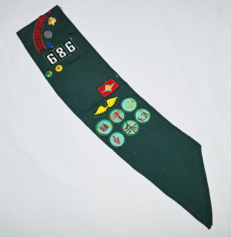 May include: Green Girl Guide sash with various embroidered badges, including a troop number "686", a "Star Gorgeno" badge, and several merit badges.
