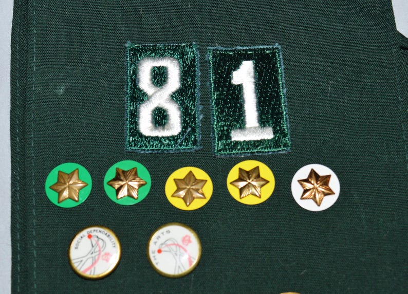 May include: A green fabric patch with the number "81" embroidered in white. There are five gold star-shaped badges on a green, yellow, and white background.