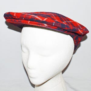 Puede incluir: Gorra plana a cuadros rojos, azules y blancos. La gorra est&aacute; hecha de una tela suave y tiene un dise&ntilde;o cl&aacute;sico. El sombrero se muestra en una cabeza de maniqu&iacute; blanca.