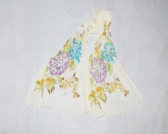 May include: A white sheer scarf with a floral print in shades of yellow, blue, and purple. The scarf has a tie at the top.