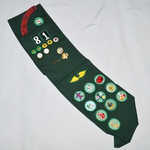 May include: A green Girl Guide sash with a red and white "Girl Guides Council" patch, a number "81" patch, and various embroidered badges.