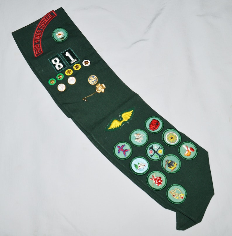 May include: A green Girl Guide sash with a red and white "Girl Guides Council" patch, a number "81" patch, and various embroidered badges.