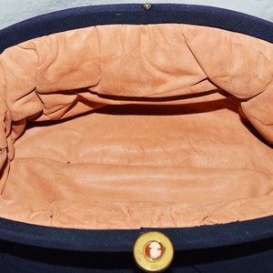 May include: A navy blue fabric clutch purse with a gold button closure. The interior is lined with a light brown fabric.