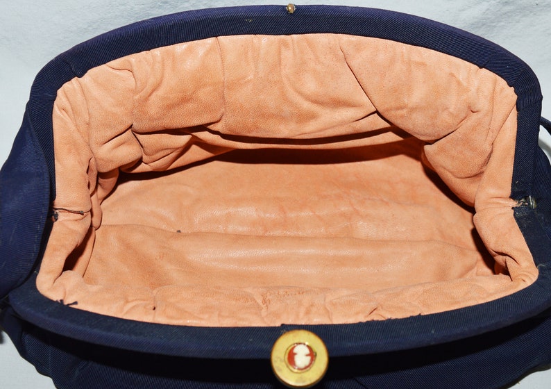 May include: A navy blue fabric clutch purse with a gold button closure. The interior is lined with a light brown fabric.