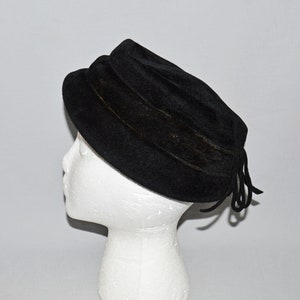 May include: A black velvet hat with a wide brim and a gathered detail. The hat has a black ribbon tied at the back.