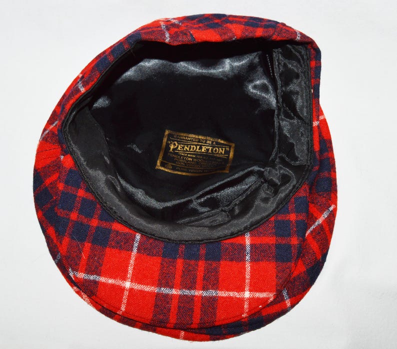 Puede incluir: Gorra de estilo newsboy a cuadros rojos, blancos y azul marino. El interior est&aacute; forrado con sat&eacute;n negro y presenta una etiqueta dorada que dice "Pendleton". Un estilo cl&aacute;sico, adecuado para diversas ocasiones.