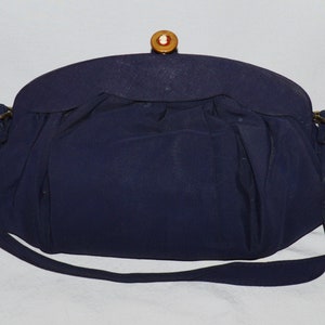 May include: A navy blue fabric handbag with a gold clasp and a decorative button. The bag has a long strap.