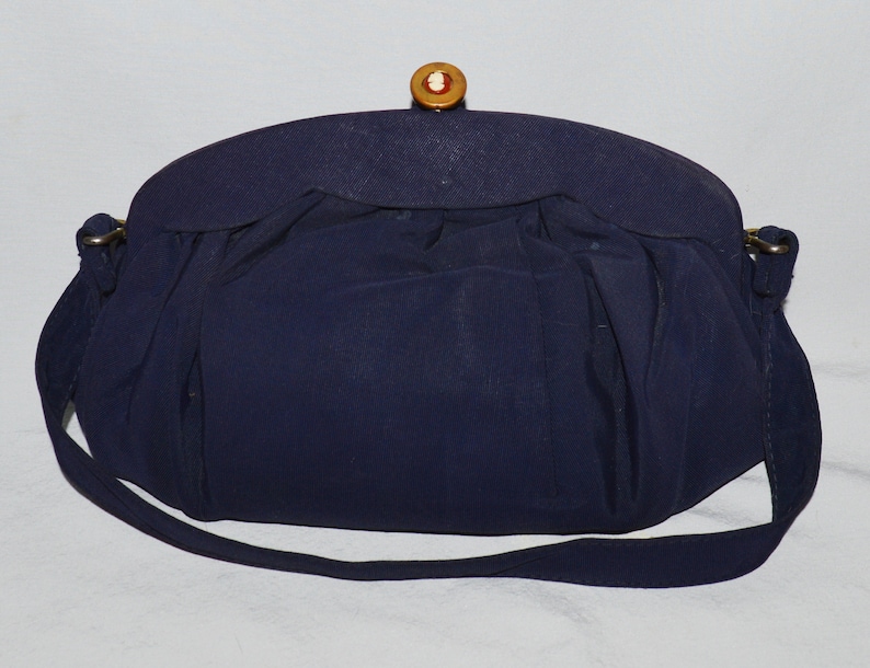 May include: A navy blue fabric handbag with a gold clasp and a decorative button. The bag has a long strap.