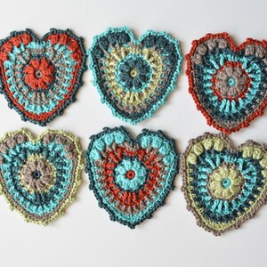 Puede incluir: Seis posavasos de coraz&oacute;n hechos a crochet en varios colores, incluyendo turquesa, verde, marr&oacute;n y rojo. Los posavasos tienen un dise&ntilde;o circular en el centro.