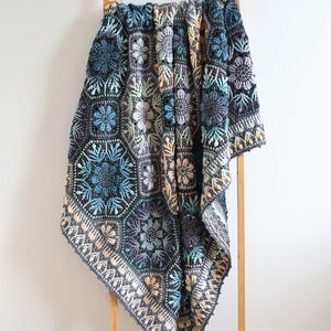 May include: A handmade crochet blanket featuring a repeating hexagonal motif pattern. The design incorporates a dark charcoal gray base with intricate floral and geometric details in shades of teal, light blue, lavender, soft yellow, and cream.