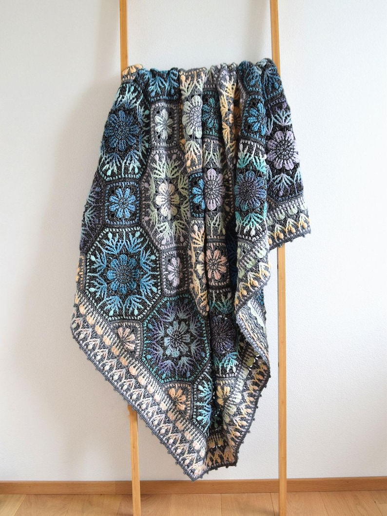 May include: A handmade crochet blanket featuring a repeating hexagonal motif pattern. The design incorporates a dark charcoal gray base with intricate floral and geometric details in shades of teal, light blue, lavender, soft yellow, and cream.
