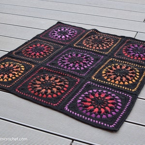 May include: A black crochet blanket with a repeating pattern of colorful circles. The circles are made with a gradient of orange, pink, and purple yarn.